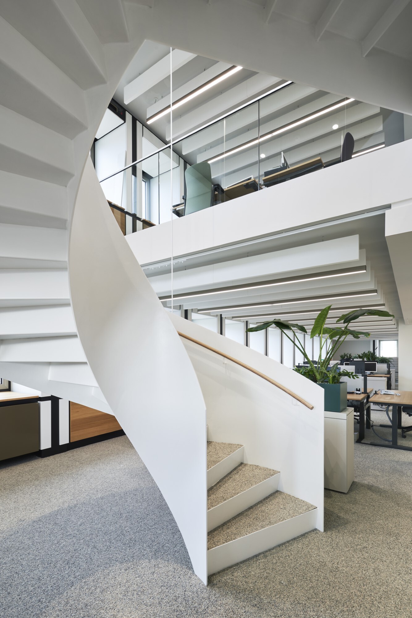 Wendeltreppe mit Metallgeländer und Blick nach oben in ein Großraumbüro mit Akustikbaffeln an der Decke.