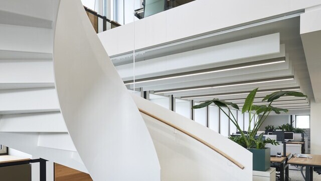 Wendeltreppe mit Metallgeländer und Blick nach oben in ein Großraumbüro mit Akustikbaffeln an der Decke. | © Constantin Meyer | Reichel Architekten
