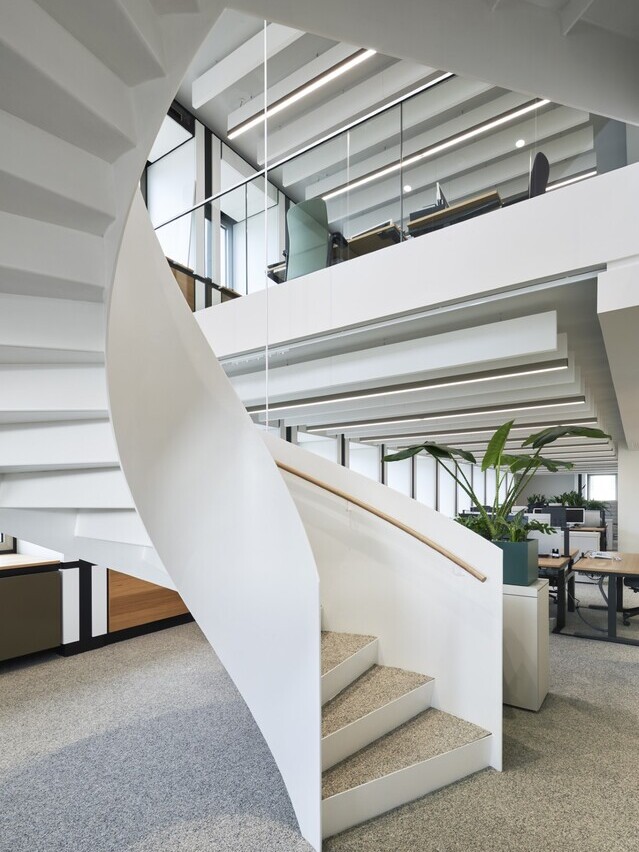 Wendeltreppe mit Metallgeländer und Blick nach oben in ein Großraumbüro mit Akustikbaffeln an der Decke. | © Constantin Meyer | Reichel Architekten