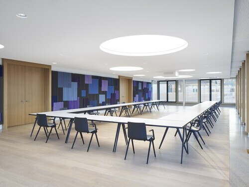 Conference room with a large U-shaped arrangement of tables, the walls are graphically designed in shades of blue, round light ceilings are distributed around the room in the white ceiling.
