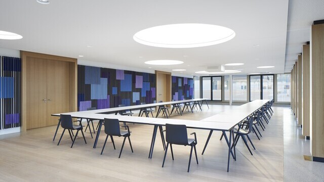 Conference room with a large U-shaped arrangement of tables, the walls are graphically designed in shades of blue, round light ceilings are distributed around the room in the white ceiling.