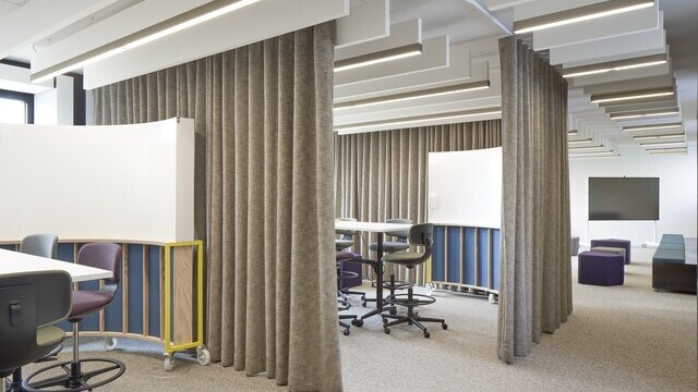 New Work workshop area with room units that can be separated by curtains; linear acoustic baffles are arranged in rows on the ceiling throughout.
