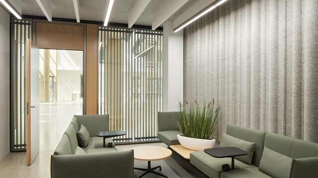Cosy waiting area in a separate room furnished with green sofas, white acoustic baffles on the ceiling and linear lights in a row.