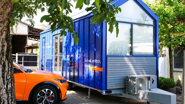 A modern blue tiny house with a large window, air conditioning, and a trailer hitch. | © Alexander Strifler
