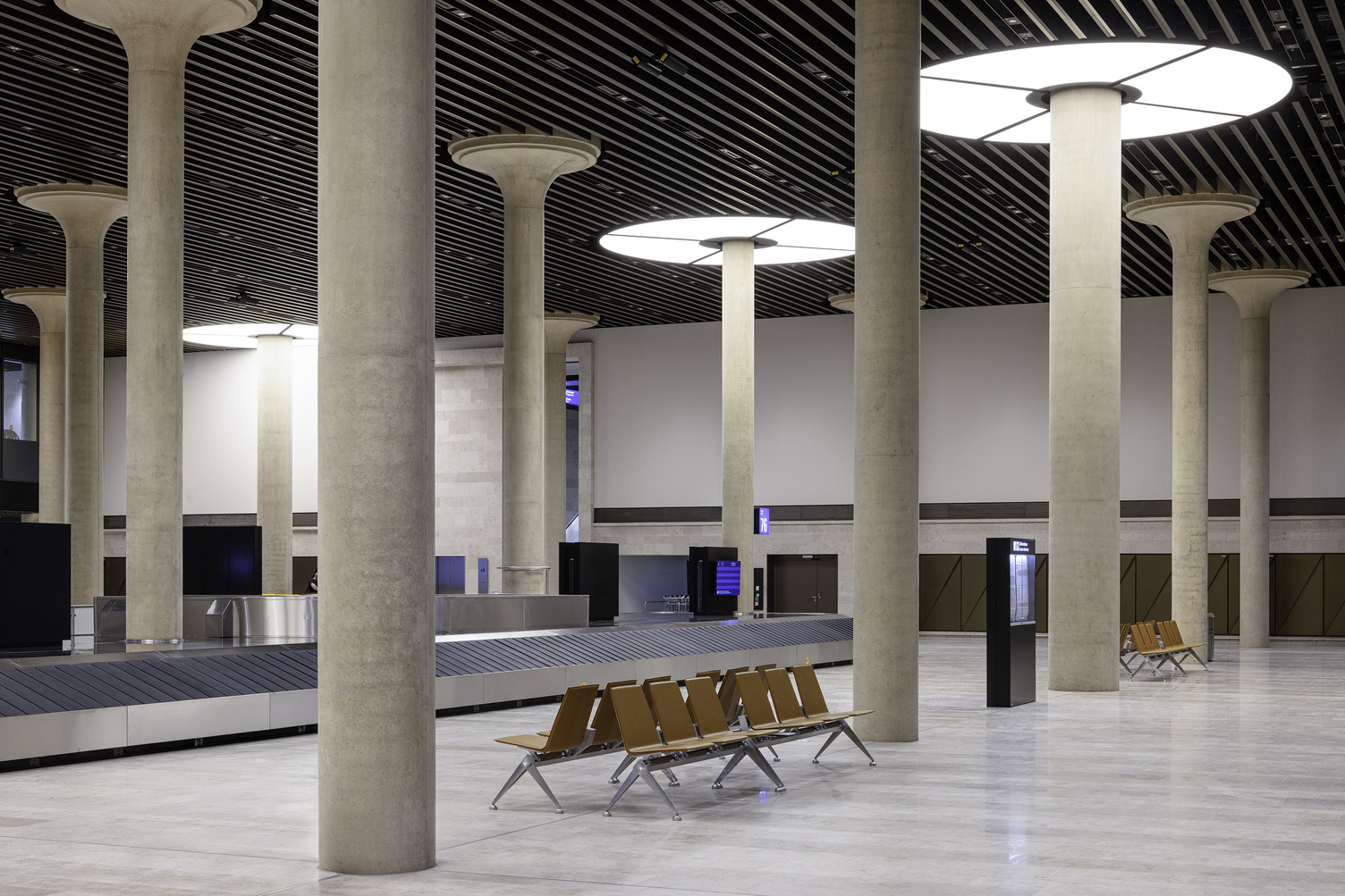 Gepäckausgabe Fraport Terminal 3 menschenleer, im Fokus Säulen mit Lichtdeckenringen darum, die je aus 4 Viertelkreissegementen bestehen.  | © Foto: HGEsch