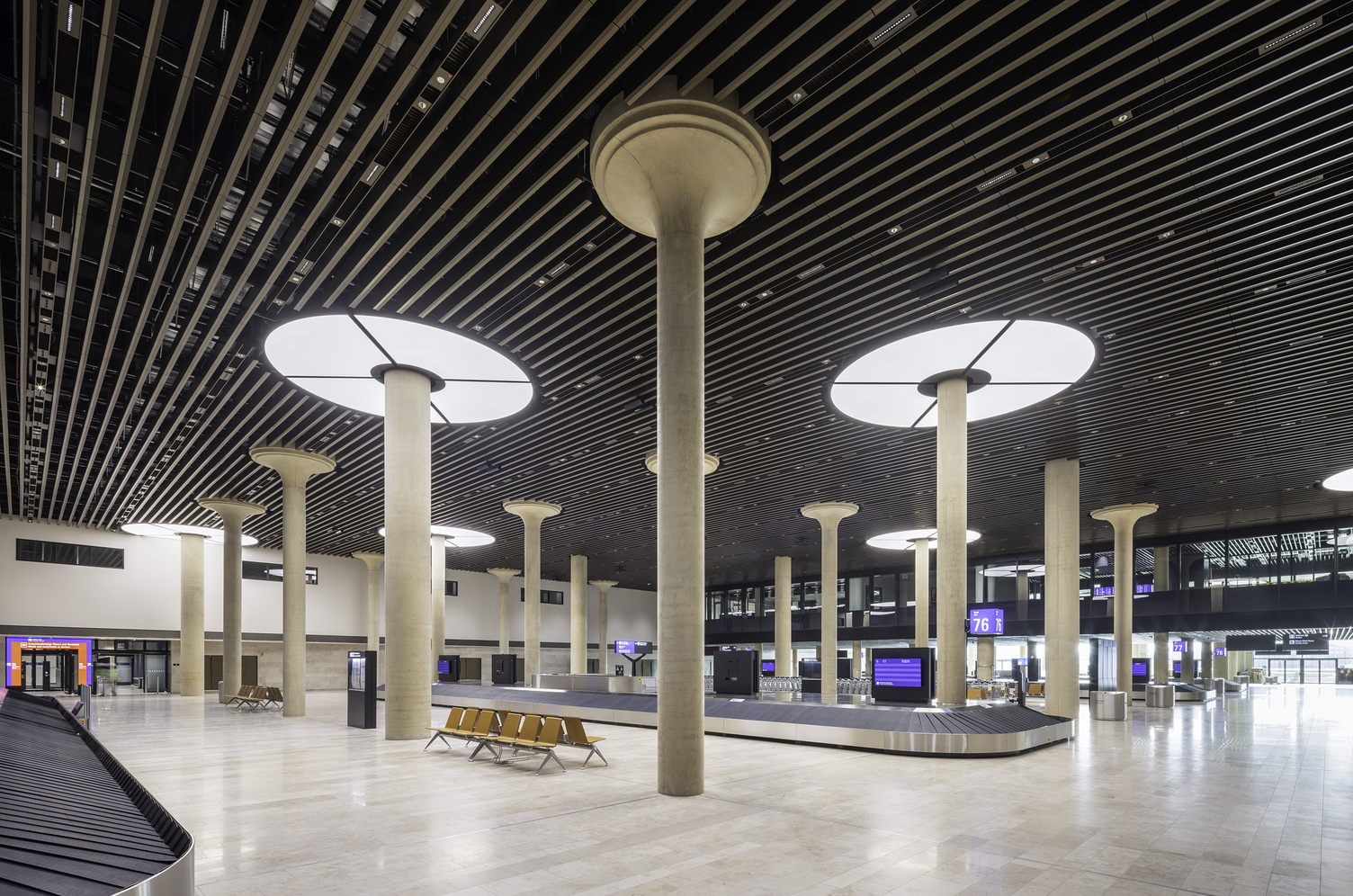 Gepäckausgabe Fraport Terminal 3 menschenleer, im Fokus Säulen mit Lichtdeckenringen darum, die je aus 4 Viertelkreissegementen bestehen.  | © Foto: HGEsch