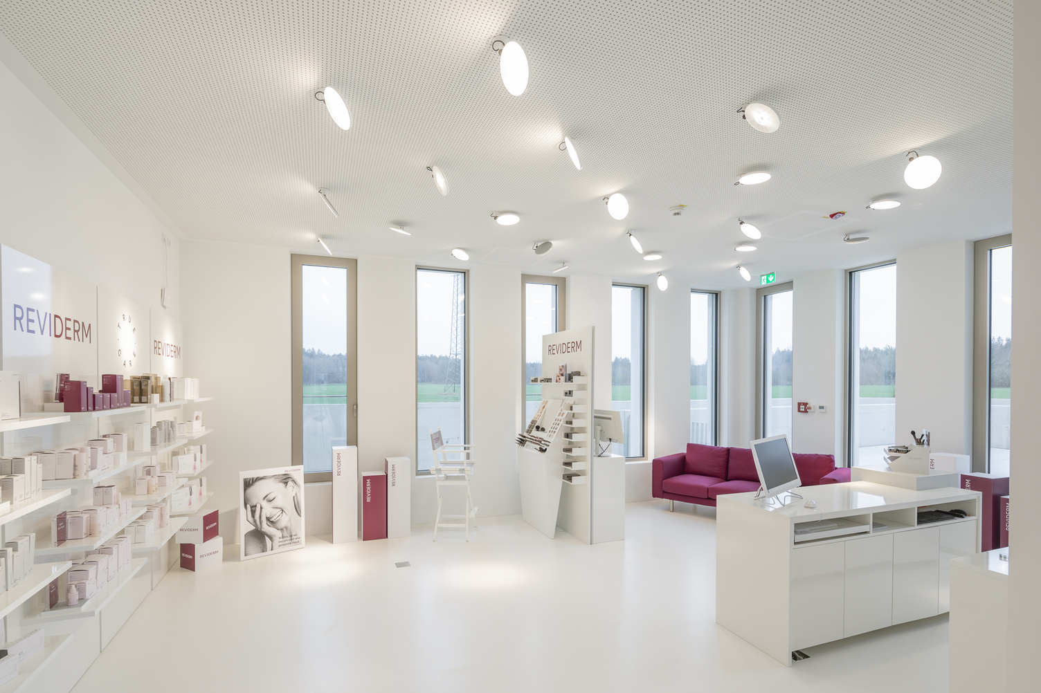 Showroom von Reviderm mit mehreren Downlights AVVENI PURE CEILING in weiß an der Decke. Weiß gehaltener Raum, rote Farbakzente durch Mobiliar. | © Michael Heinrich | www.licht.studio