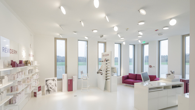 Showroom von Reviderm mit mehreren Downlights AVVENI PURE CEILING in weiß an der Decke. Weiß gehaltener Raum, rote Farbakzente durch Mobiliar. | © Michael Heinrich | www.licht.studio