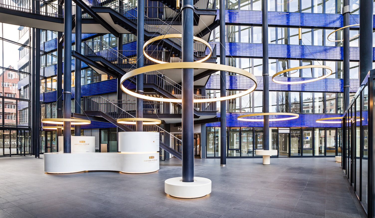 Goldene großformatige Ringleuchten, CIRCOLO I, abgependelt um die Säulen des verglasten Atriums mit blauen Wänden des Hanseforum Hamburg.  | © gerrit meier