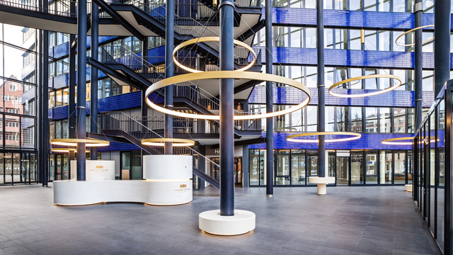 Goldene großformatige Ringleuchten, CIRCOLO I, abgependelt um die Säulen des verglasten Atriums mit blauen Wänden des Hanseforum Hamburg.  | © gerrit meier