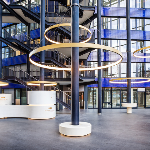Goldene großformatige Ringleuchten, CIRCOLO I, abgependelt um die Säulen des verglasten Atriums mit blauen Wänden des Hanseforum Hamburg. 