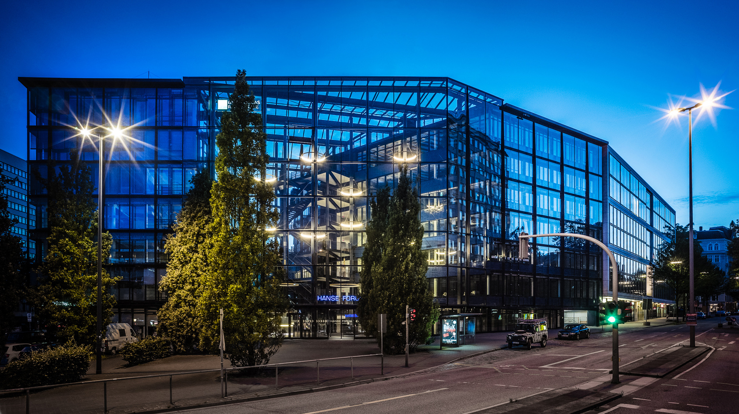 Außenansicht auf ein großes Glasgebäude in dem auf verschiedenen Ebenen Lichtringe leuchten.