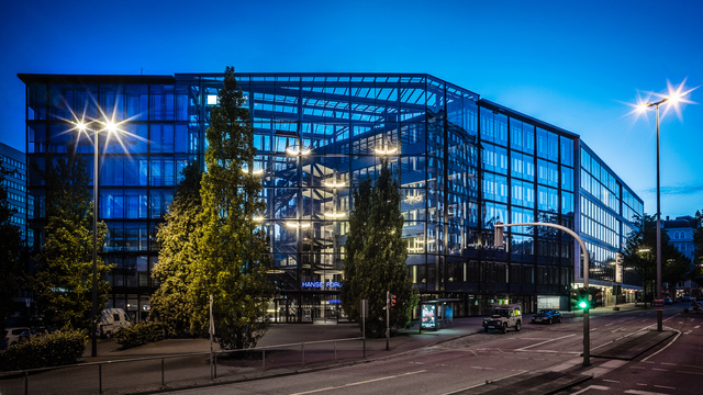 Außenansicht auf ein großes Glasgebäude in dem auf verschiedenen Ebenen Lichtringe leuchten.