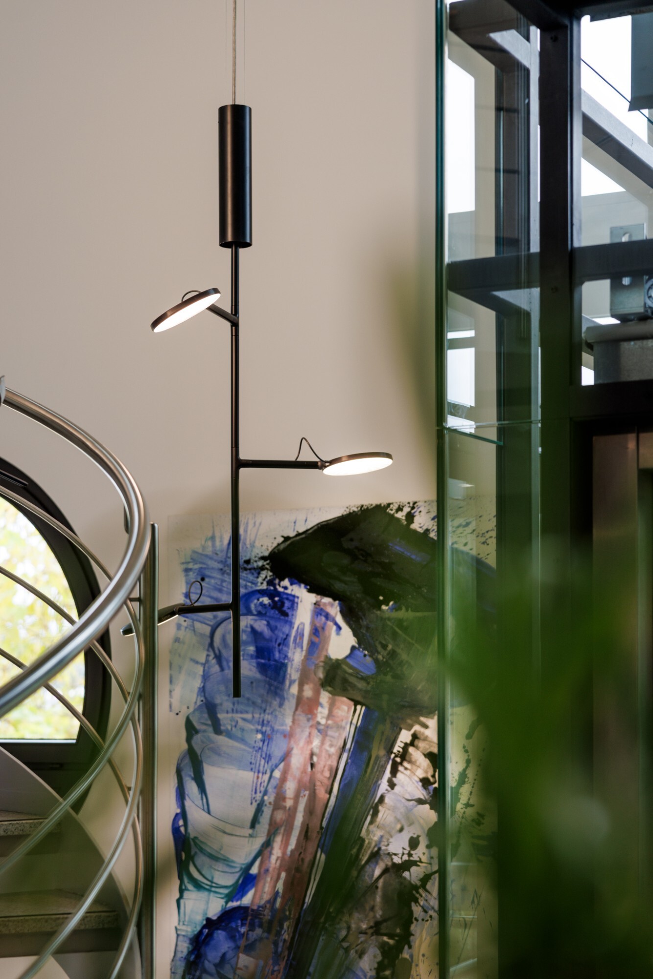 Vertikal verweigte schwarze Pendlleuchte mit Leuchtköpfen, AVVENI VERTICAL 3, vor einem bunten Wandbild, links daneben gebogenes Metalltreppengeländer. | © Tobias Fröhner Photography