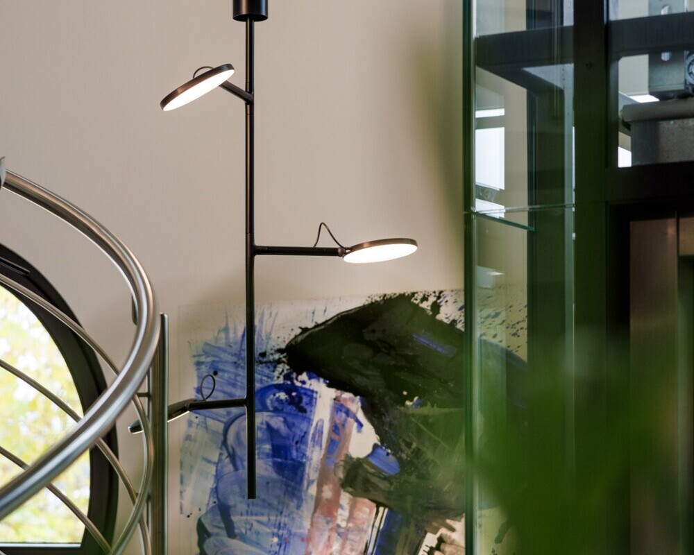 Vertical spiral movable luminaire heads | © Tobias Fröhner Photography Vertically tilted black pendant luminaire with light heads, AVVENI VERTICAL 3, in front of a colourful mural, to the left of it a curved metal stair railing. | © Tobias Fröhner Photography