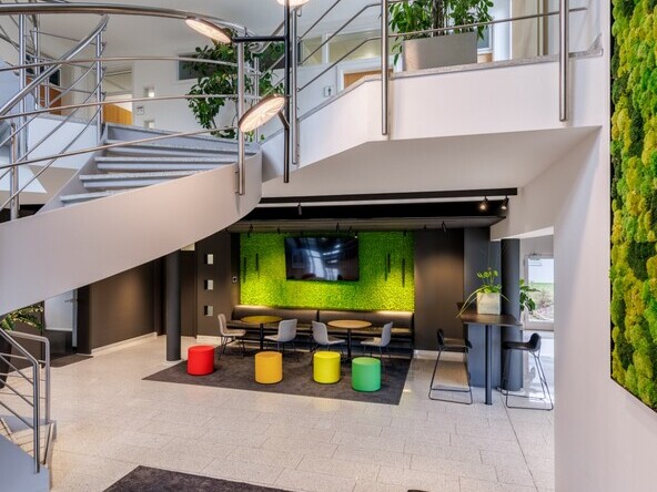 Entrance area with staircase and various zones with lounge furniture. In the centre of the picture is a vertically branched tube light with light heads. | © Tobias Fröhner Photography