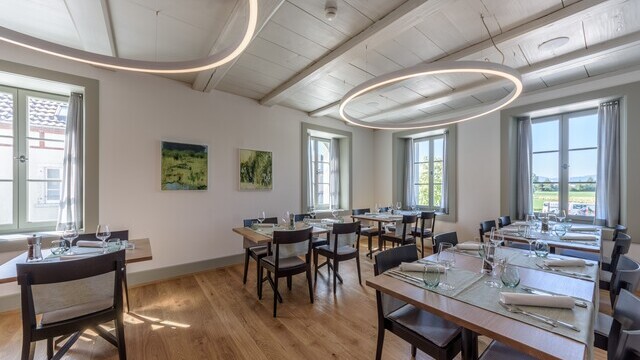 Elegant and cosy restaurant room in the Hirschenbad Langenthal, invitingly laid tables, white wooden ceiling from which large, narrow, directly illuminated white ring lights (DUETTO) are suspended. | © LUXED
