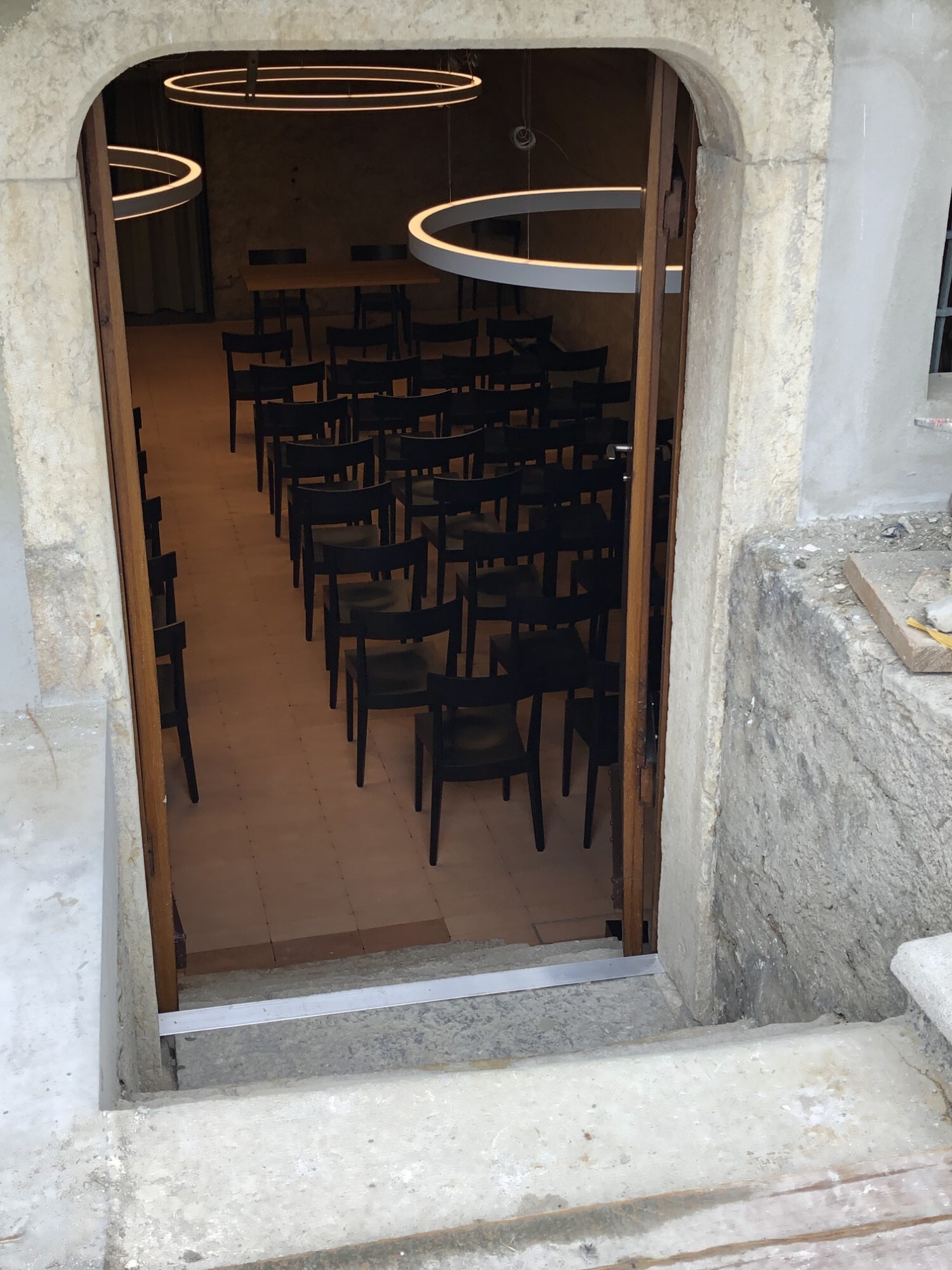 View through an entrance door into a large room with seating and white ring lights (DUETTO) suspended above the chairs.