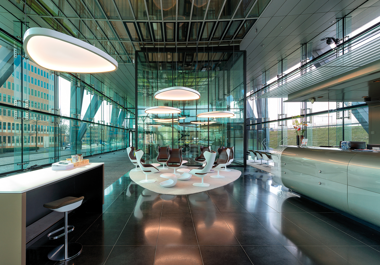 Soft Delta L+A over seating areas of a lobby | © SATTLER | Nathalie Peters Fabric-covered Soft Delta Light & Acoustic luminaires from SATTLER in a modern glass lobby with reception and cafeteria | © SATTLER | Nathalie Peters