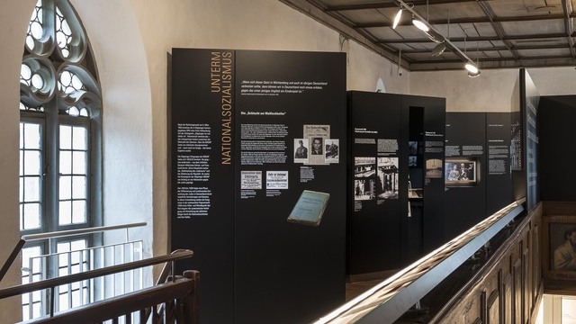 Museum exhibition in a dark wooden setting. Black information panels and architectural features such as antique chandeliers are illuminated by AVVENI’s flexible, adjustable round lighting heads. | © Rose Hajdu, Stuttgart