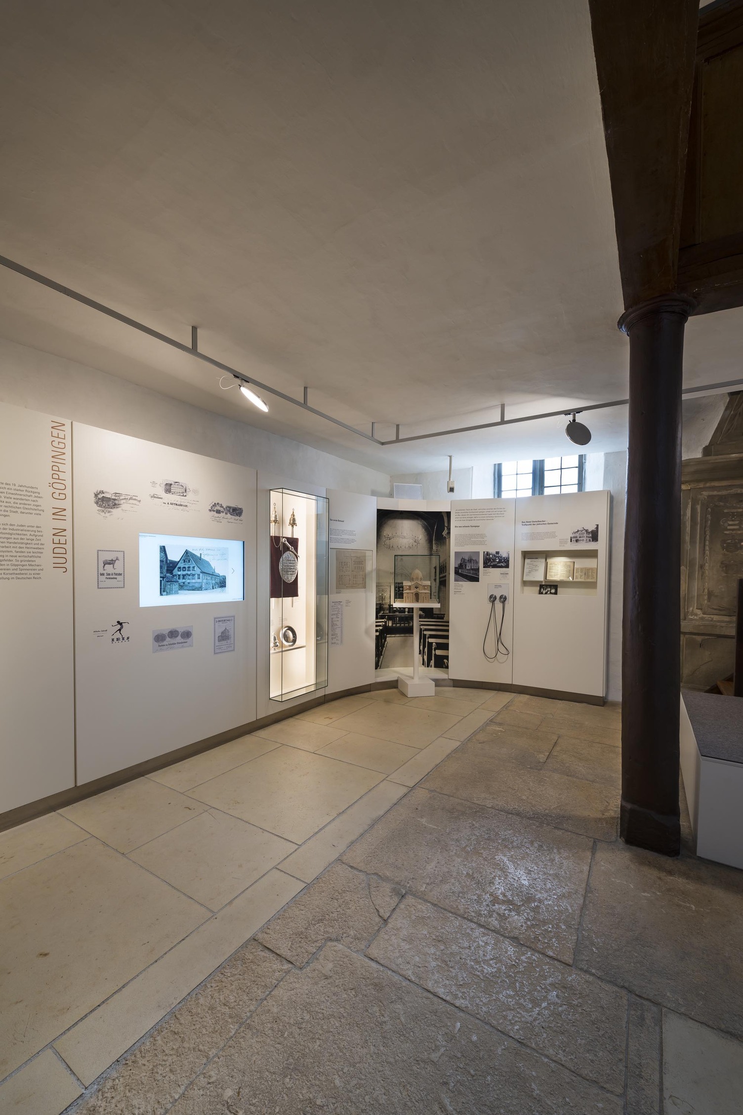 Durchgängiges Lichtkonzept. Ausstellungsbereich mit hellen Informationstafeln und hellem Fließen-/Steinboden. An der Decke ein Anbau-Track-System das entlang des Raumes auch um ein Eck weiterführt, in der Stromschiene flache, runde bewegliche AVVENI-Leuchtenköpfe.  | © Rose Hajdu, Stuttgart