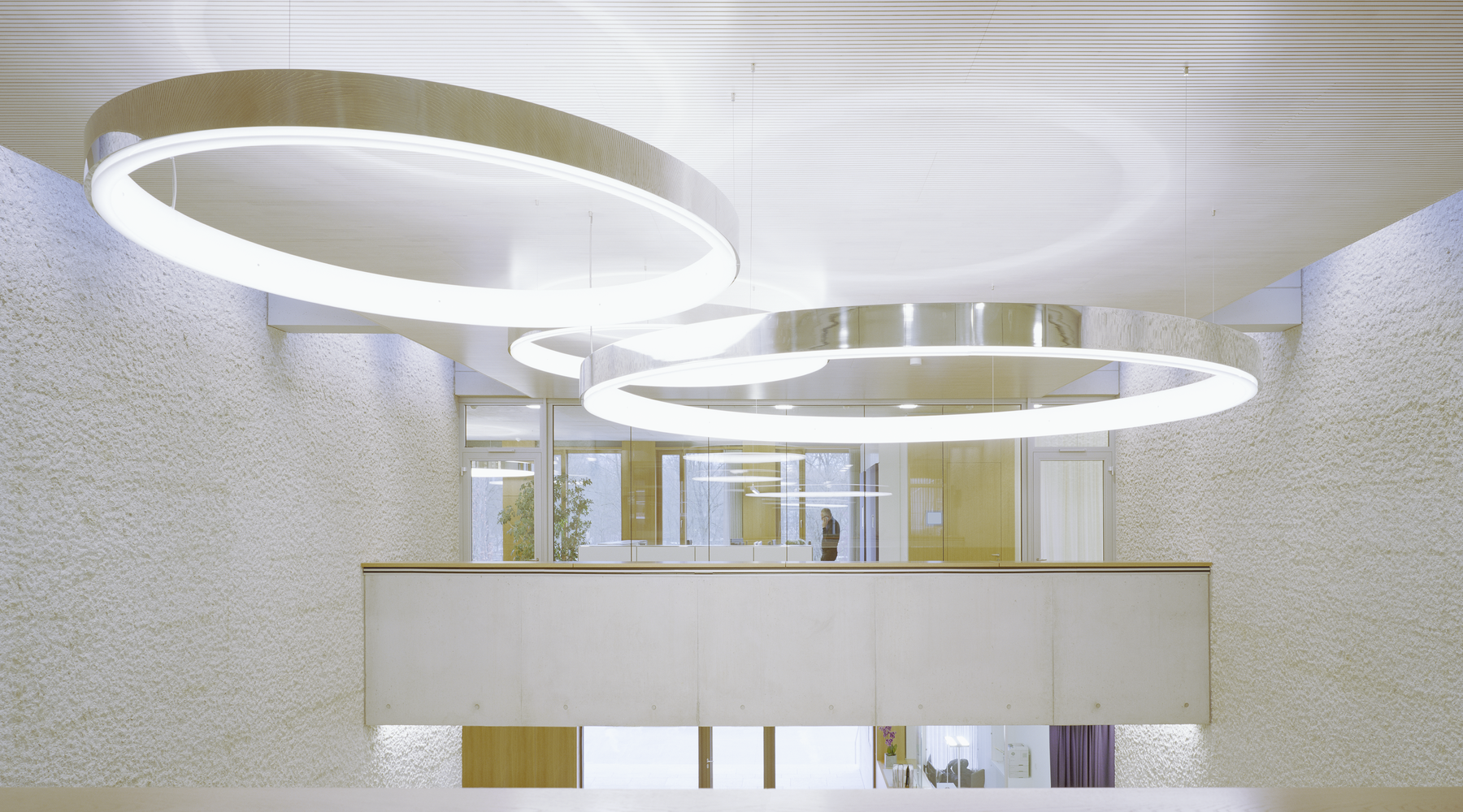 Ringleuchten im Sichtbetongebäude der Karl Köhler GmbH | © Brigida González Drei großformatige CIRCOLO Ringleuchten in Aluminium poliert als Mittelpunkt im Sichtbetongebäude kombiniert mit hellen Holzelementen der Karl Köhler GmbH. Deckennah aufgehangen auf Höhe 1. OG des verglasten Büros. Unter den Leuchten freier Raum als Veranstaltungsraum nutzbar. | © Brigida González