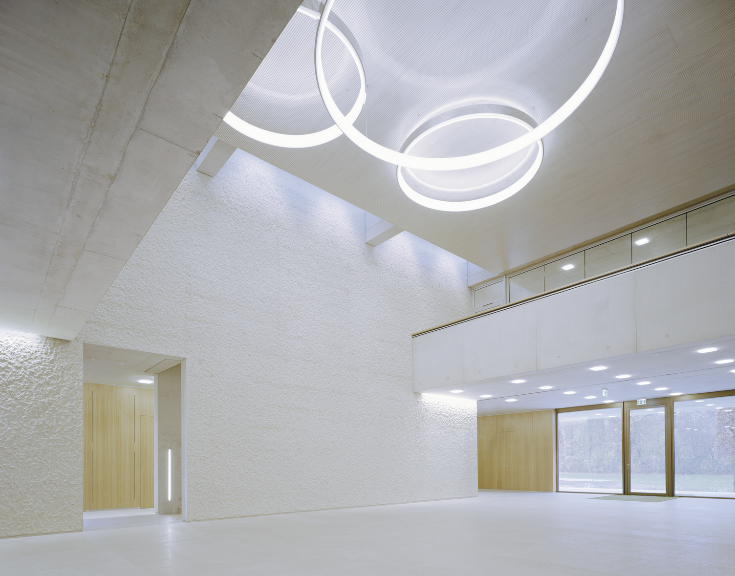 Blick von unten an die Decke eines Sichtbetongebäudes, mittig im zweigeschossigen hohen Raum hängen auf freier Fläche 3 Ringleuchten CIRCOLO in Aluminium poliert, auf beiden Seiten verengt sich der Raum um ein Stockwerk.