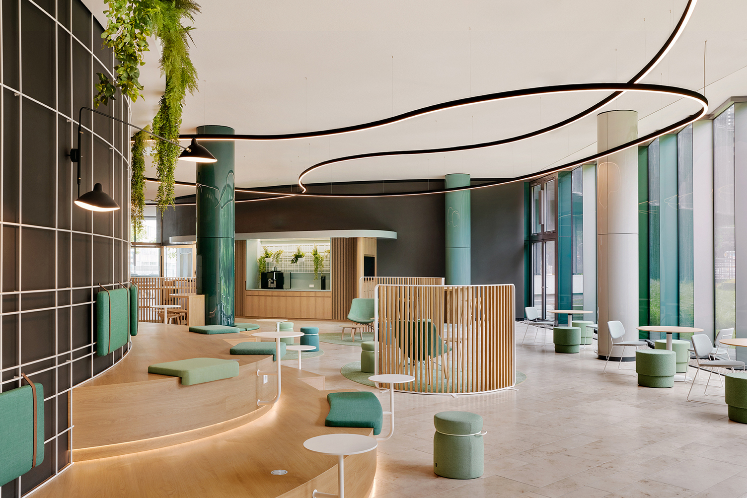 Lichtlinien DUETTO in der Lounge KfW Westarkade Frankfurt Moderner Lounge-Bereich mit grünen runden Säulen, halbrunder Treppenholzbank, grünen Kissen, Pflanzen deckennah und gebogenen schwarzen DUETTO Lichtlinien, die teils um die Säulen verlaufen.