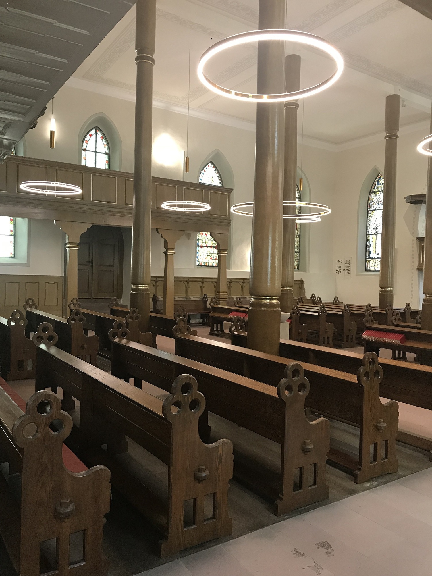Church lighting: Golden ring lights providing direct and indirect illumination with a pendant canopy Chancel of a historic church with stone walls and pillars, wooden benches and golden, directly and indirectly illuminated DOPPIO ring lights.