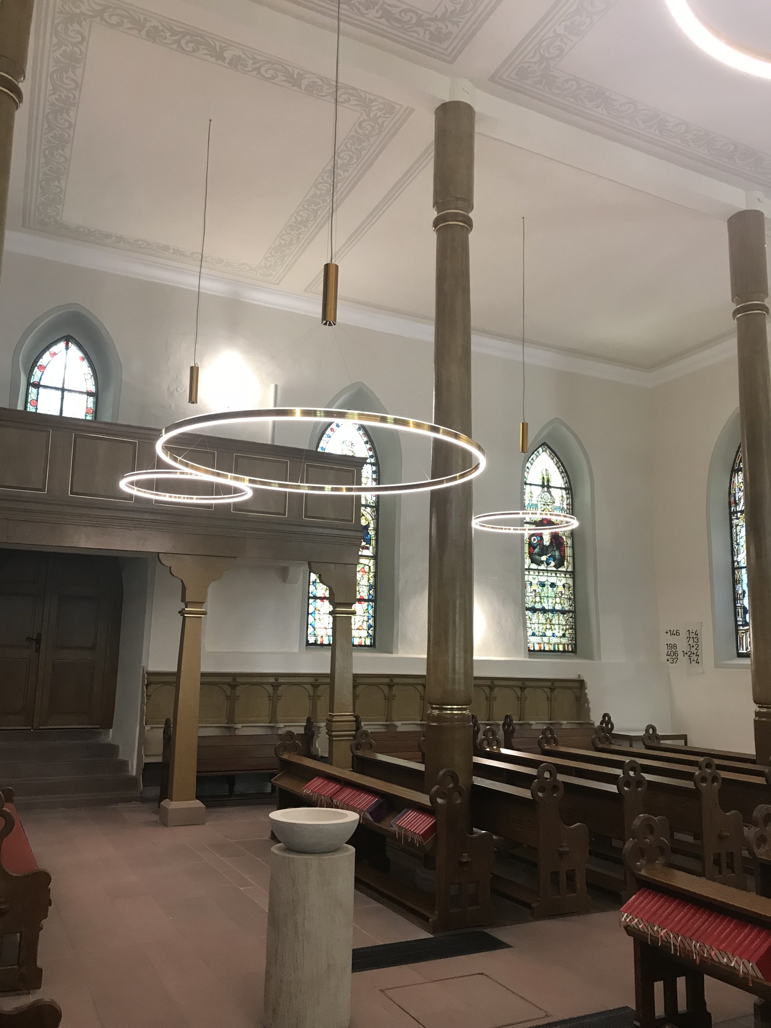 Ringleuchten DOPPIO im Kirchenraum der ev. Kirche Westhofen Altarraum einer historischen Kirche aus Steinmauern und Säulen, sowie Holzbänken und goldenen direkt und indirekt leuchtenden DOPPIO Ringleuchten.