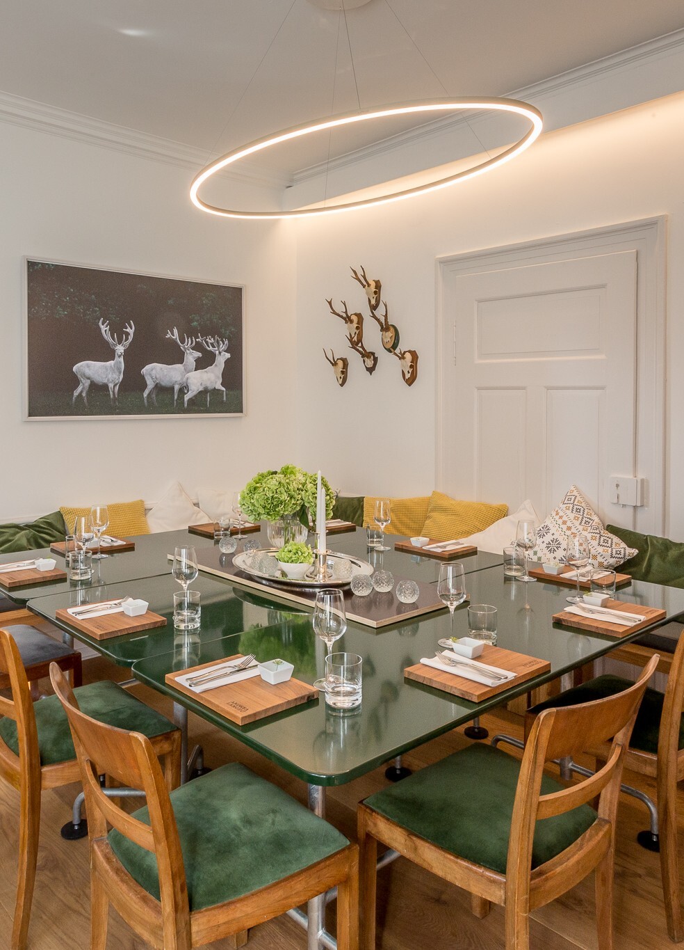 Schmale SLIM ELLIPSE elliptische Pendelleuchte direkt leuchtend über einem quadratischen fein gedeckten Esstisch im Gastraum der Kochschule Andrea Lange