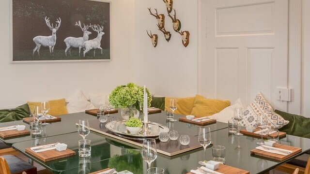 A slim SLIM ELLIPSE elliptical pendant light, casting direct light over a square dining table set with fine tableware in the dining area of the Andrea Lange cookery school | © LipsiART digital photography, René Krause