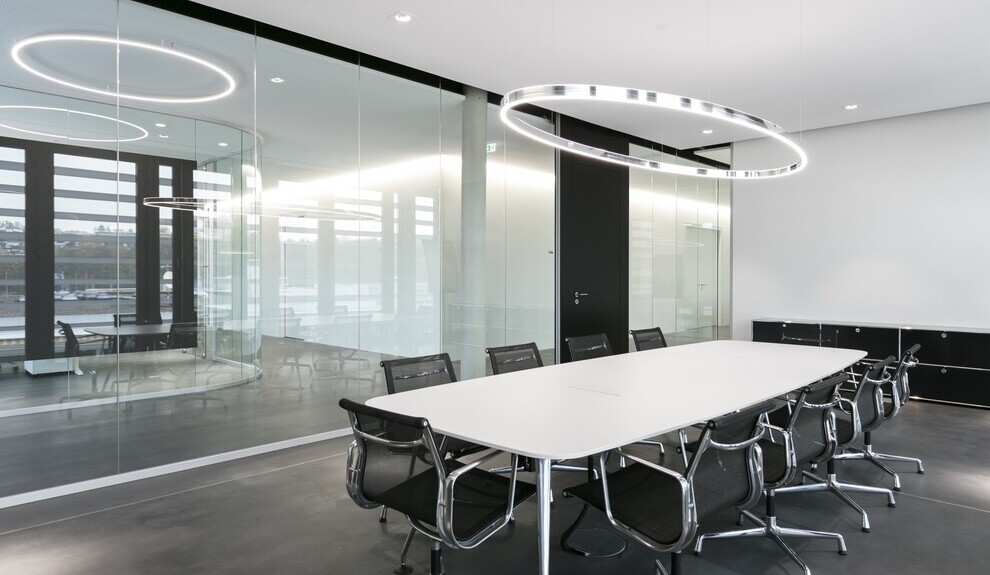 Doppio Ellipse with BE2 spotlights, each by SATTLER, arranged in a glass meeting room above a white table in a wider perspective