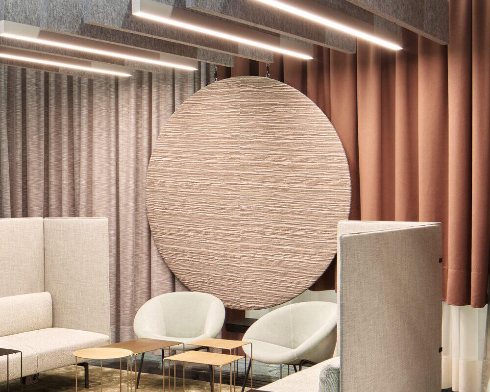 Akustisch wirksame Raum-in-Raum-Lösung mit BAFFELLEUCHTEN | © Philip Kottlorz Messestand ORGATEC 2024 von Walter Knoll mit hellen Polstermöbeln und kleinen Sofa-Tischen, darüber sind mehrere lineare Baffelleuchten (BAFFELLEUCHTE) und reine lineare akustisch wirksame Baffeln (ACOUSTIC BAFFLE) in grau abgependelt. | © Philip Kottlorz