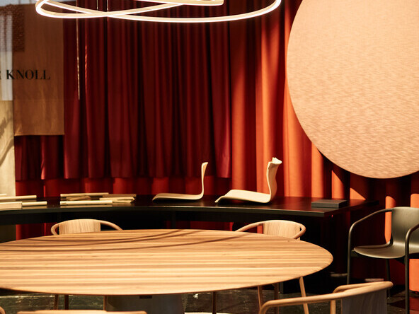 WALTER KNOLL trade fair stand at ORGATEC with a round wooden table and wooden chairs around it, with three interlocking ring lights, the PURE MOTION, hovering above it. | © Philip Kottlorz