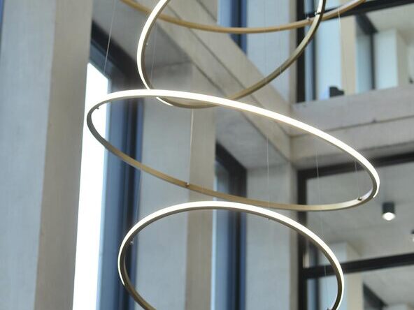 Close-up of various SLIM OUT slim ring lights suspended from the ceiling at different heights and angles throughout the room. Installation by SATTLER in the foyer of the Monari headquarters | © monari