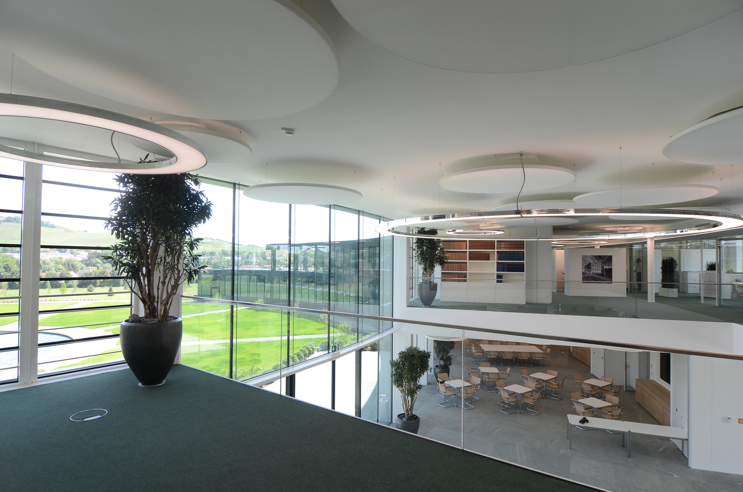 Anello und Acoustic Lights von SATTLER in Kombination in einem Foyer | © SATTLER | Werbe-und Medienagentur Mohring Blick von einer Empore in ein modernes Foyer mit Glasfront. Ausgestattet wurde das Foyer mit Anello Leuchten, stoffbespannte Akustik Panele, jeweils von SATTLER. | © SATTLER | Werbe-und Medienagentur Mohring
