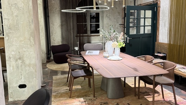 A wooden dining table with wooden chairs by WALTER KNOLL in a shabby-chic room; suspended above the table is a modern EVOLUTION M chandelier, comprising cylindrical elements in a champagne gold finish. In the background, rounded, luminous triangular SLIM DELTA direct lights can be seen. | © SATTLER