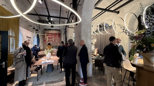 A shabby-chic room featuring numerous arched openings, bustling with people admiring SATTLER lighting and Walter Knoll furniture at the Munich Design Days 2026. Pendant lights, floor lamps, chandeliers and more from SATTLER are on display, arranged alongside tables, sofas and armchairs by Walter Knoll. | © SATTLER