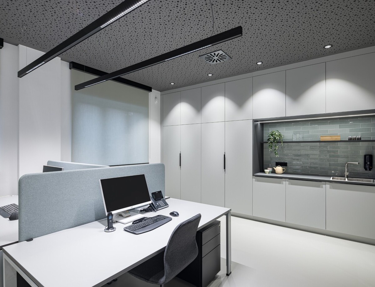 Dreier Arbeitsplatz mit zwei PALADIO LENS Linearleuchten über den Schreibtischen und BE Downlights an der Decke am Rand als Grundbeleuchtung und um die umliegenden Wände bzw. Schränke auszuleuchten.