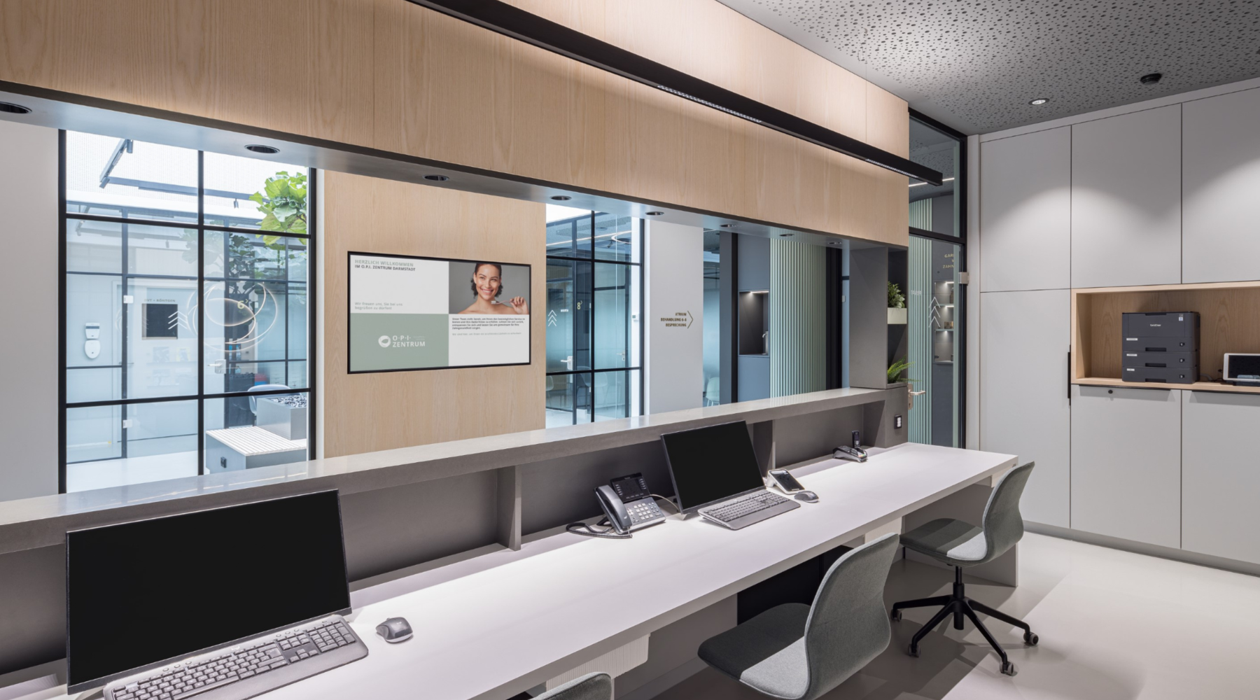 PALADIO linear luminaire for the reception desk of a medical practice Reception desk of a medical practice with a view from the workstations to the corridor, with glare-free PALADIO LENS linear luminaires above the monitor workstations and BE spotlights on the ceiling by the neighbouring cabinets.