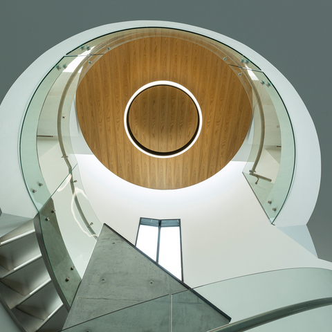 View upwards in a stairwell with a glass handrail and a round outward-radiating luminaire, CIRCOLO INVERSE (diameter 1600), in the centre of the wooden ceiling.