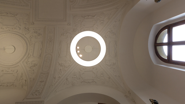 Blick von unten auf eine großformatige Pendel-Ringleuchte ANELLO, die gleichzeitig die Gewölbe-Stuck-Decke & die Exponate beleuchtet. | © Bayerische Schlösserverwaltung, Residenz München