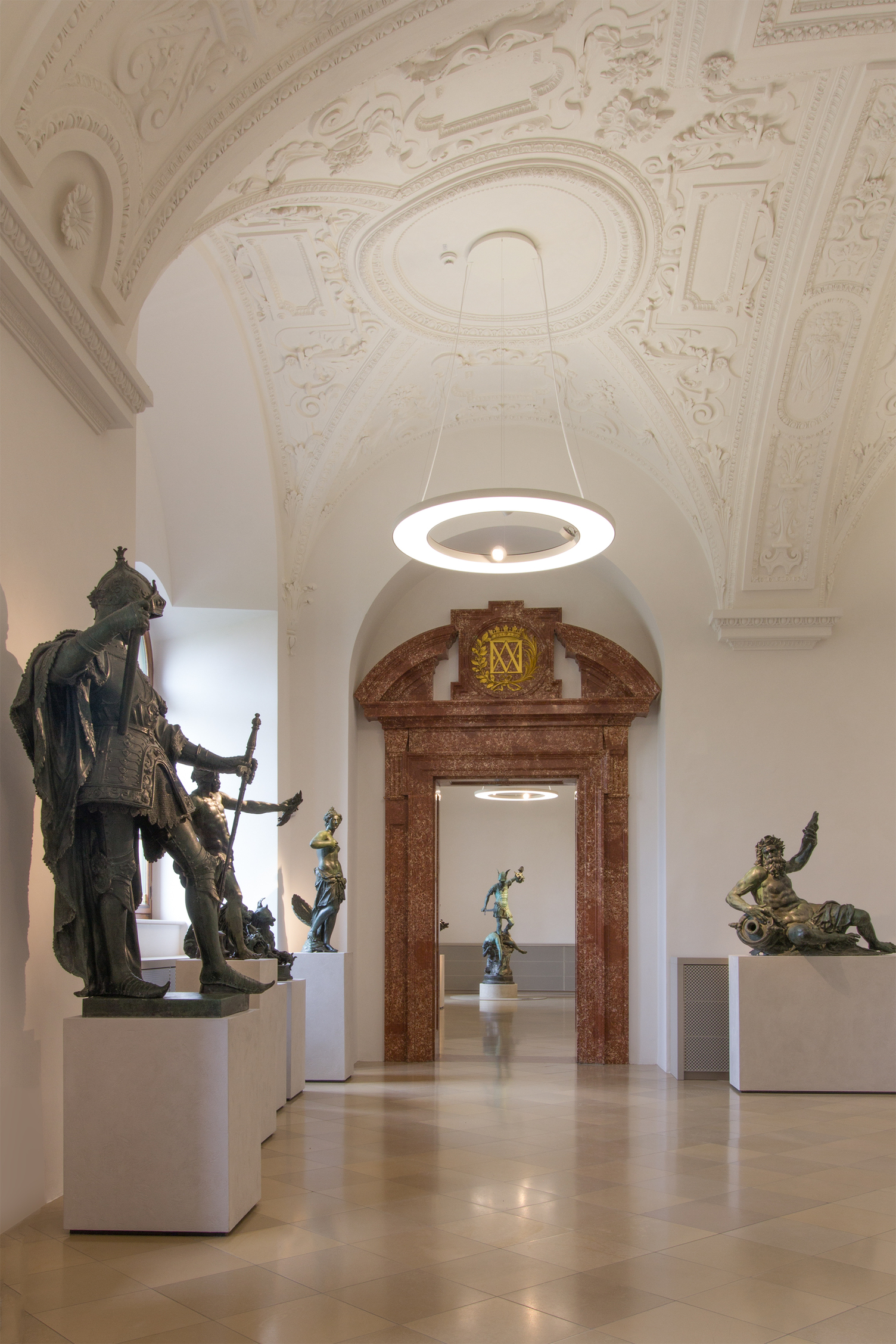 Bronzestatue der Residenz München - Ringleuchte ANELLO Bronzestatue wacht über den Flur der Residenz München und gibt den Blick zum Marmor-Durchgang und einer grooßformatigen Ringleuchte frei.
