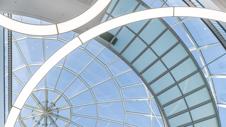 A view from below of a glass dome at the Rhön-Klinikum. A detail showing two large-format, wide-area ring lights from SATTLER’s ANELLO series, suspended from the glass roof.