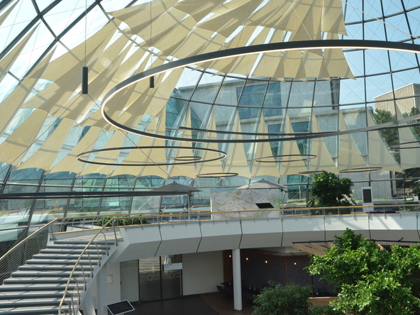 A large, open staircase beneath a circular glass roof at the Rhön-Klinikum. The focus is on ring lights of various sizes with black housings, suspended at different heights throughout the room. 