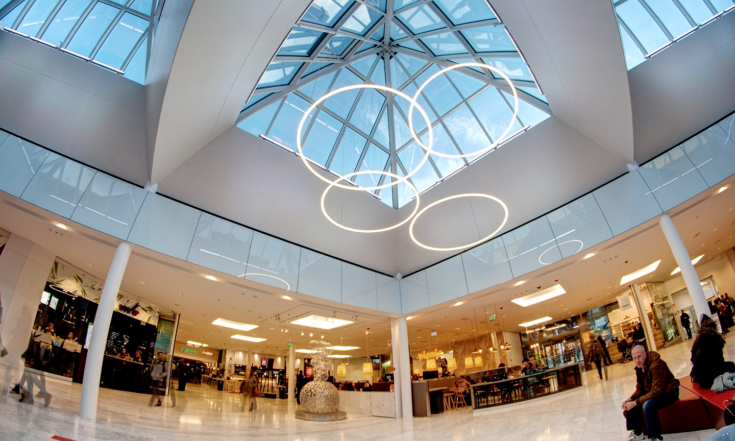Multiple SLIM ring luminaires in different heights form a striking lighting object under the glass roof of Helsinki shopping mall.