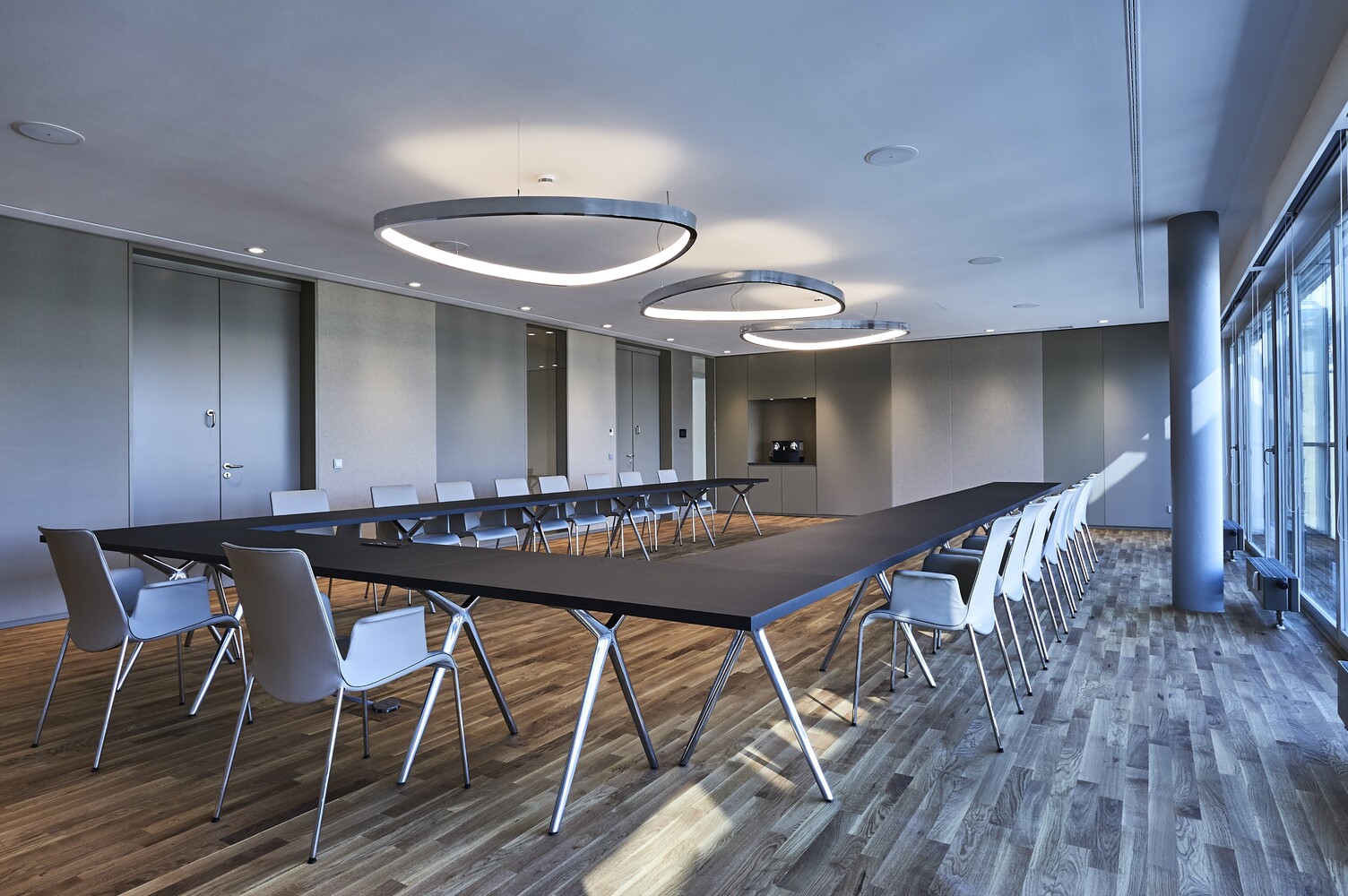 Eleganter Veranstaltungsraum mit großformatigen Ringpendelleuchten und moderner Bestuhlung für Meetings und Konferenzen.