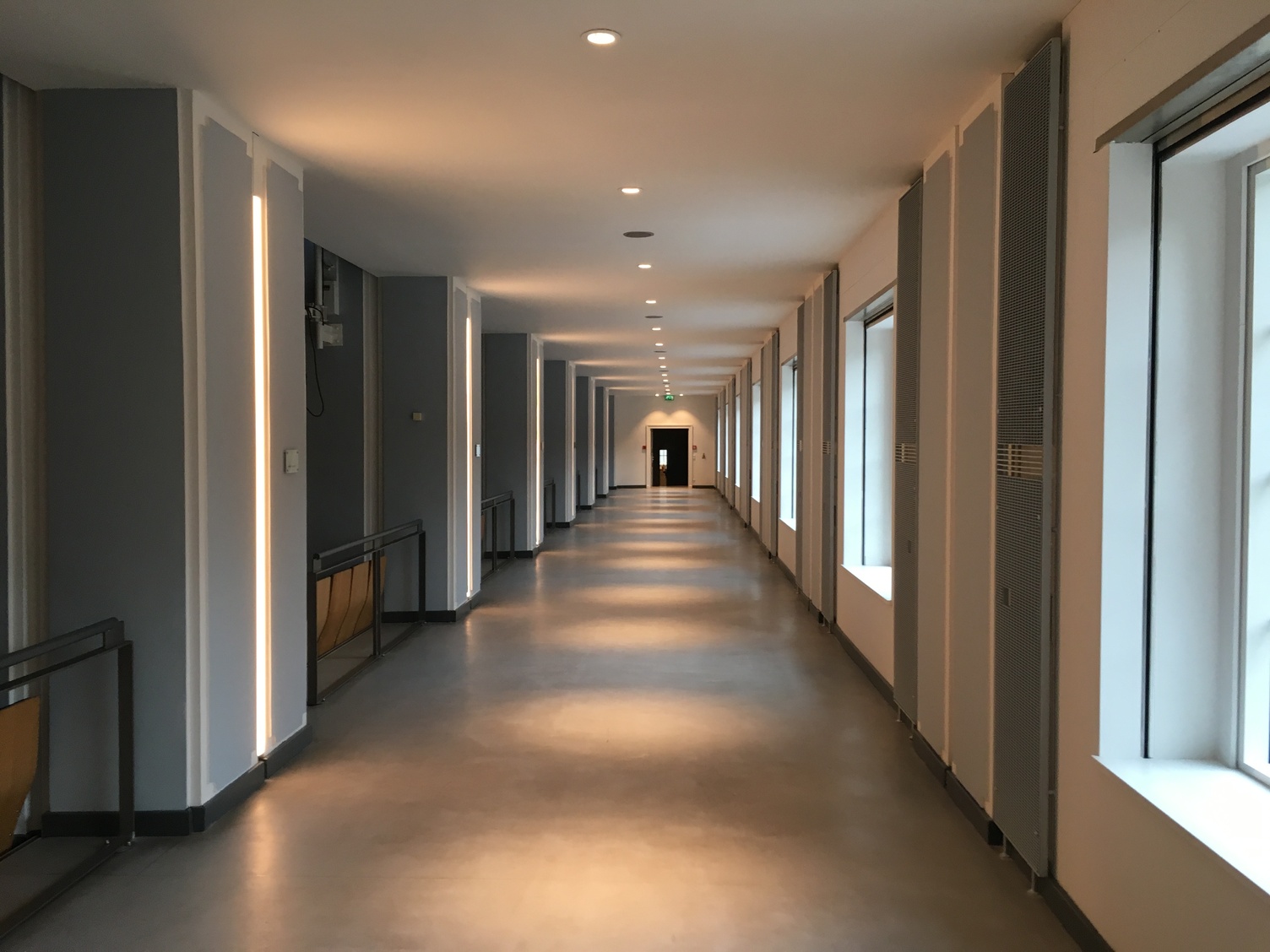 A corridor above the visitors’ seating area in Kassel Town Hall. Lighting refurbishment using SATTLER lighting solutions. The corridor features blue columns with recessed light channels, and several round spotlights from the BE Downlight series mounted on the ceiling.