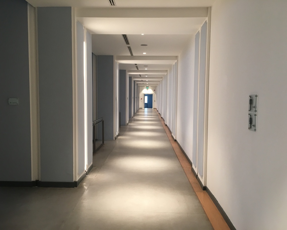 Bright hallway in Kassel City Hall. The spectator stands are on the left. A light is incorporated into the columns. Round BE downlights are also installed along the ceiling of the corridor, providing pathway lighting.